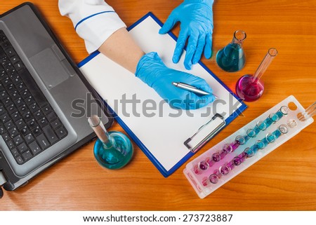 assistant of writes beside the laptop and test tubes with reagents