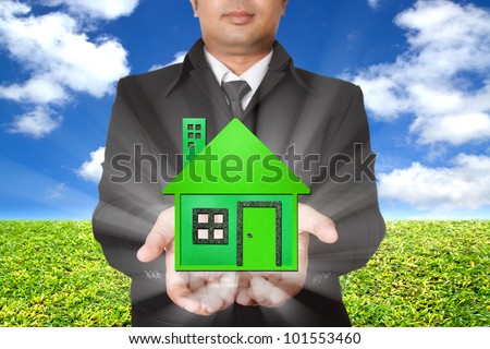 businessman shows a green house with blue sky