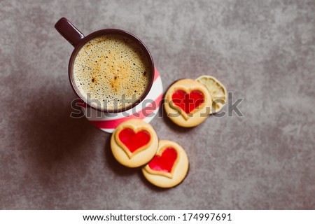 A cup of coffe standing on a table with some cookieis with heart-shaped red jam. Good morning! Lovers\' breakfast