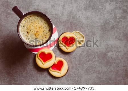 A cup of coffe standing on a table with some cookieis with heart-shaped red jam. Good morning! Lovers\' breakfast