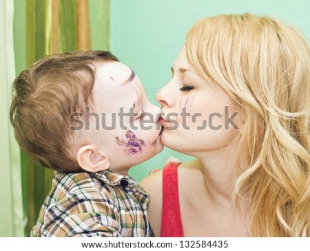 Mother and son with paints on faces kissing to each other