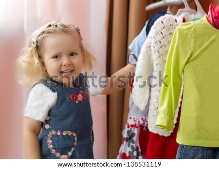 Adorable joyful little girl choosing  clothes