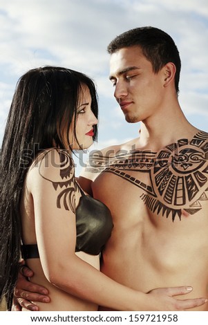 Young couple against blue sky with ancient ethno tattoo