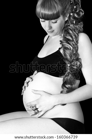 Black and white photo of pregnant happy woman on black