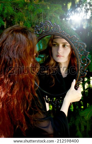 Beautiful girl witch in black dress with old mirror