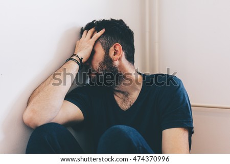 Sad young man sitting in the corner of the room