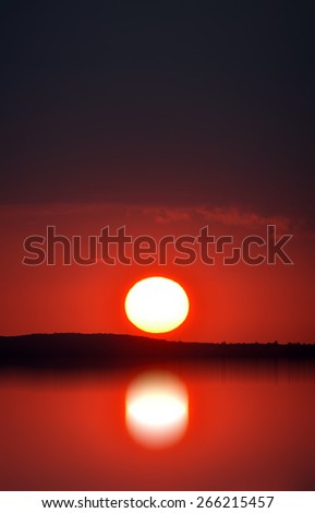 Red sunset over the mountains. Sun reflection in the water.