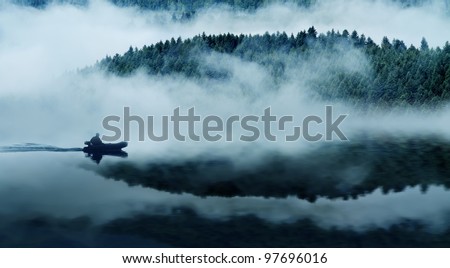 Quiet mountain lake in a thick fog. In the background a mountain forest. Floats on the water in the boat people. The blue tone.