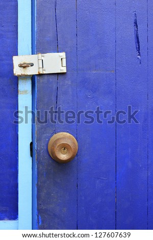 An old rusty door knob on blue wooden door, focus on the knob.