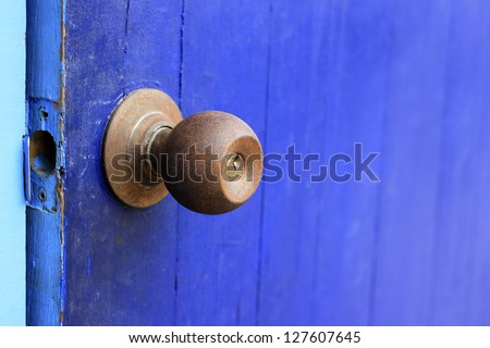 An old rusty door knob on blue wooden door, focus on the knob.