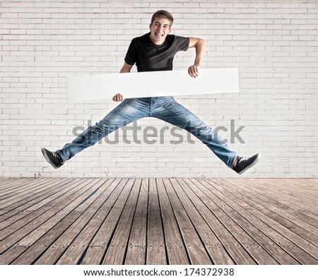 attractive young man jumping with a white banner on a room with white bricks wall and wood floor