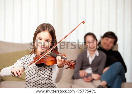 little girl playing violin with her family at home