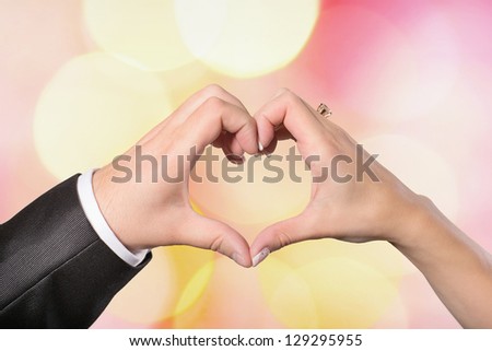 Hands bride and groom in a heart shape on a colored background defocused