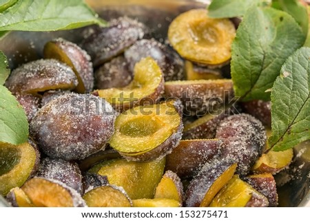 Detail view on halved plums in bowl sprinkled with sugar with green leaf