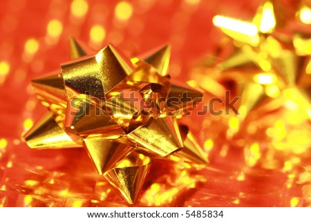 Shiny gold gift bow on gold metallic wrapping paper with reflected back-lighting