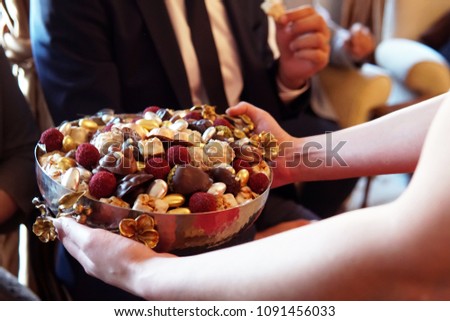 sweets like confectionery and chocolates served by a girl, dressed red, to elder people, a traditional ceremony for ramadan feast or sacrifice feast known as eid al-adha
