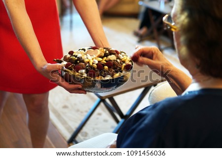 sweets like confectionery and chocolates served by a girl, dressed red, to elder people, a traditional ceremony for ramadan feast or sacrifice feast known as eid al-adha