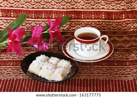 Thai tradition dessert with banana stuff and coconut slices topping and tea cup.