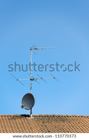 Aerial and satellite dish on roof of house with clear blue sky above