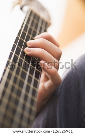 Strings and fingers of young man playing a chord on a wooden acoustic guitar
