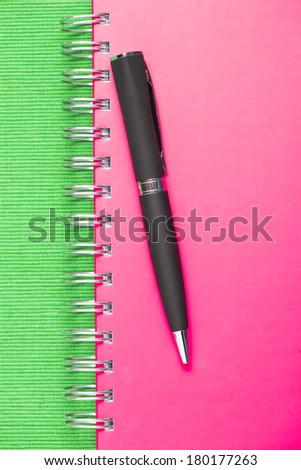 Closed pink notebook with black pen lying on top