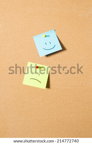 Post it notes with happy and sad face on cork message board