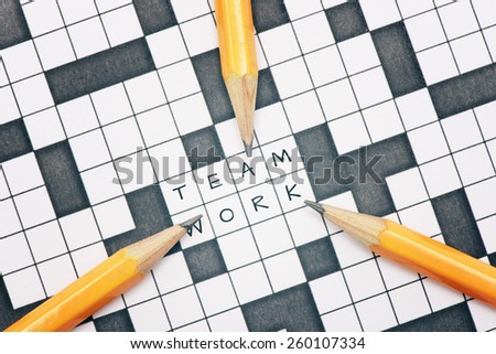 Closeup of crossword puzzle and three pens pointing to the word teamwork. Conceptual image of problem solving, finding solutions and teambuilding.