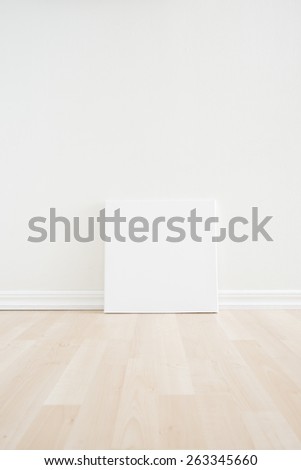 Empty room interior with artwork picture frame standing on wooden floor. Bright white scandinavian design and clean contemporary architecture. The room works as backdrop for new office or a gallery.