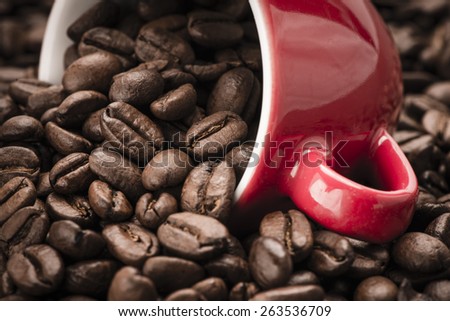 Closeup of dark roasted coffee beans spilling from a red cup. Food and drink backdrop showing aromatic and beautiful coffee beans.