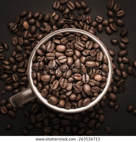 Closeup of dark roasted coffee beans in a cup viewed from above. Food and drink backdrop showing aromatic and beautiful coffee beans.