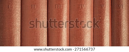 Close-up of red vintage leather books in series on bookshelf. The volumes are numbered.