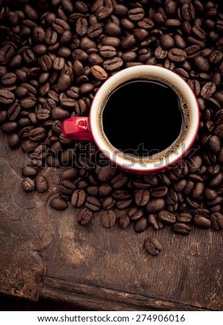 Closeup of dark roasted coffee beans and a red cup filled with fresh hot coffee. Food and drink backdrop showing aromatic and beautiful coffee beans. Can be used as a conceptual image for breakfast.