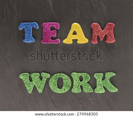 The word teamwork in colorful letters on black stone background. Conceptual image of working together, reaching goals and cooperation.