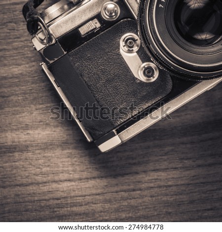 Top view of old retro 35 mm film camera lying on wooden table. Photographic nostalgia with old-fashioned photo equipment. Concepual image of old technology with a vintage look.