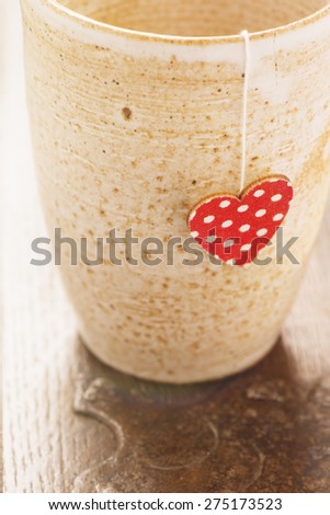Closeup of a cup of tea with a heart shaped teabag on rustic wooden table. Food and drink backdrop showing a mug of hot beverage served.