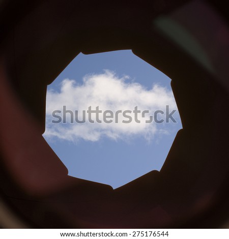 A single white cloud on a blue sky seen through the lens and aperture of a camera. Conceptual image of view on cloud computing, digital communication and storage.