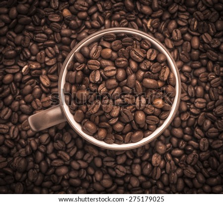 Closeup of dark roasted coffee beans in a cup viewed from above. Food and drink backdrop showing aromatic and beautiful coffee beans.