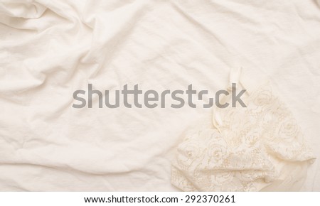 Empty crumpled white bed sheet and white silk lingerie.