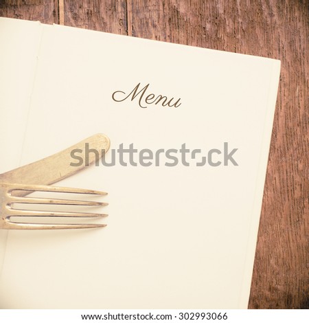 Open book on wooden table with blank white pages.  Title text with the word menu. Knife and fork on top.