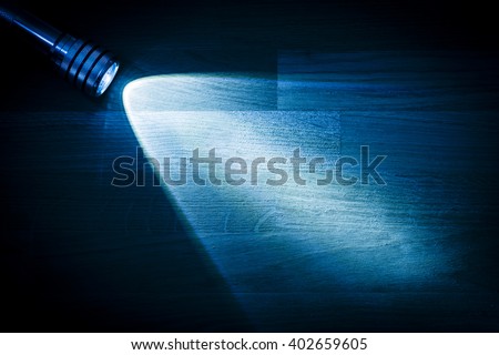 Flashlight and a beam of light in darkness. A modern led lamp with bright projection on dark wood table. Surface with copy space.