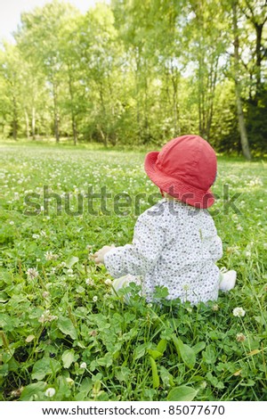 Baby girl sitting in meadow watching the nature