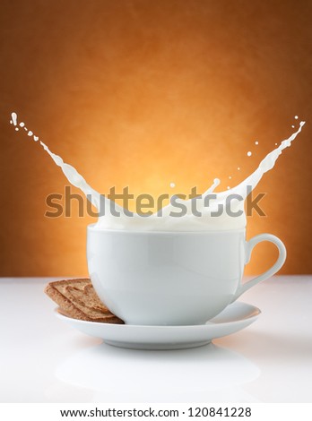 cup of milk splash with biscuit and orange background