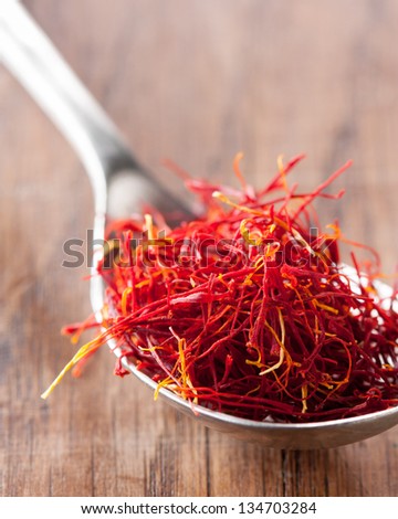 Red saffron close-up on a spoon over a wooden table