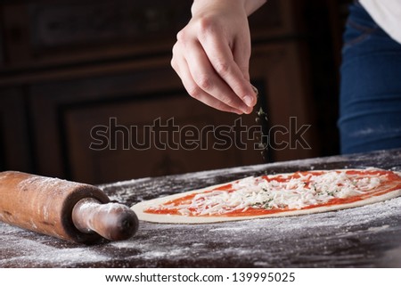 Cook putting oregano over tomato and mozzarella on a raw pizza