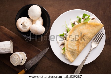 Cheese and mushrooms crepe with salad on wooden table overview