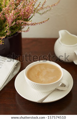 Coffee with milk on a sunday morning table with a newspaper and plant