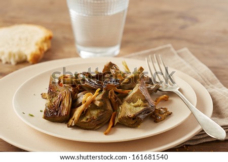 Dish of sauteed artichokes and yellow foot mushrooms on wooden table