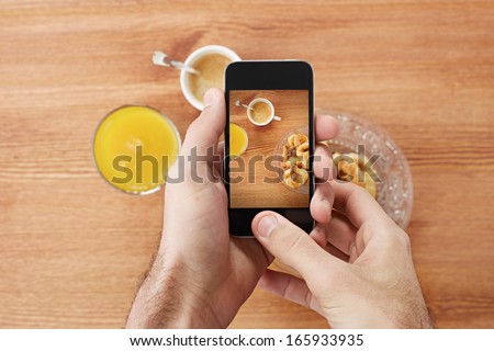 Hands taking photo of breakfast including croissants, cofee and orange juice with smartphone