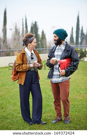 Hipster couple talking and drinking coffee to go at university campus