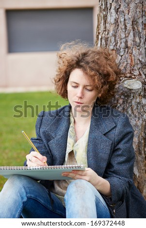 Female redhead art student drawing outdoors at college campus